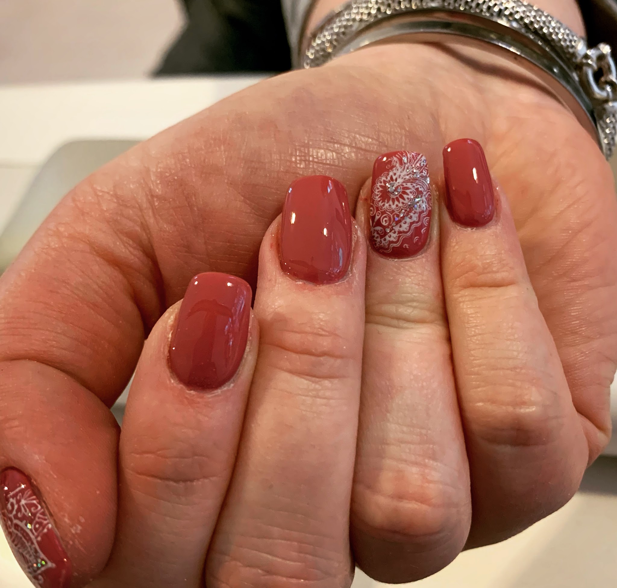 Hand met terracotta nagels en een accentnagel met wit kantmotief