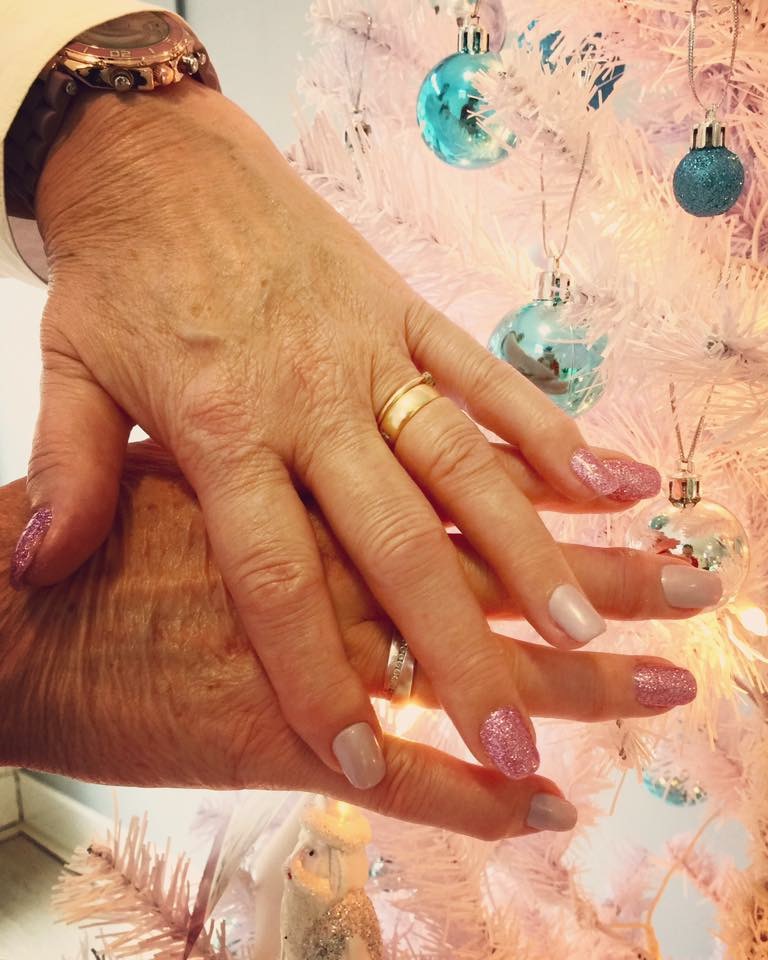 Twee handen met zachtroze en glitternagels voor een witte kerstboom